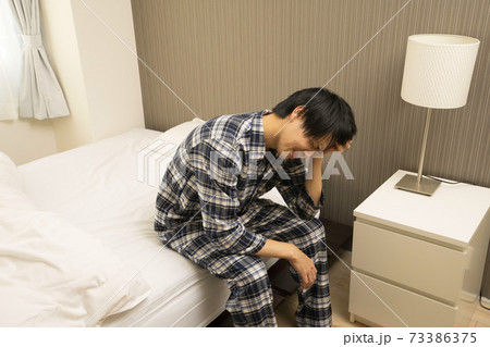 寝起きに発熱がわかり、体調が悪くなって会社に行けないパジャマ姿の男性	
